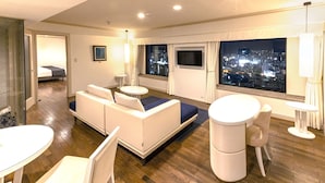 Une chambre d’hôtel moderne avec un canapé, deux petites tables rondes, un téléviseur et une vue sur la ville.