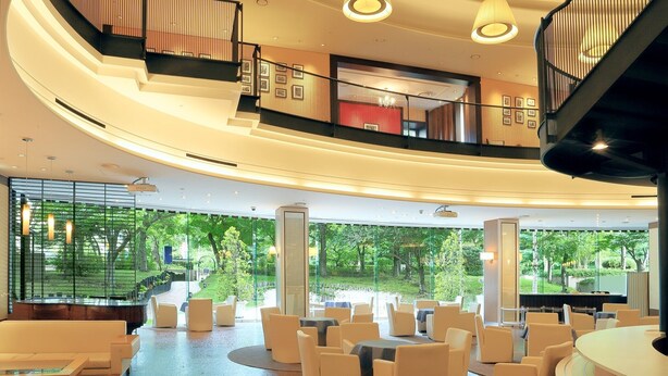 Un hall d’hôtel moderne doté d’un escalier à volutes, d’espaces aménagés pour s’asseoir et de grandes fenêtres offrant une vue sur la verdure environnante.