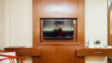 Habitación de hotel con un mueble de madera, un televisor montado en la pared, una mesita con hervidor, tazas y una botella de agua.
