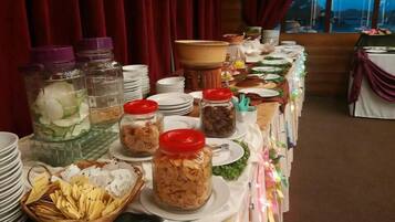 Una mesa de buffet con diversos alimentos en frascos y cestas, platos apilados y vistas al exterior a través de una ventana.