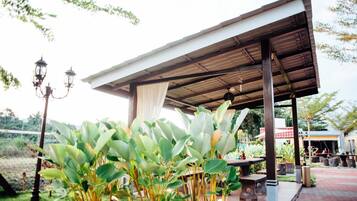 An outdoor covered patio area with a metal roof, surrounded by lush greenery and a fence.