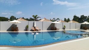 Piscina con sillas de descanso y sombrillas, rodeada por un muro alto y palmeras.
