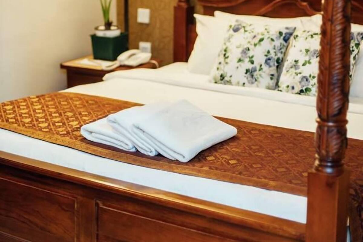 A four-poster bed with a wooden frame, a patterned bedspread, and a folded towel on the footboard.