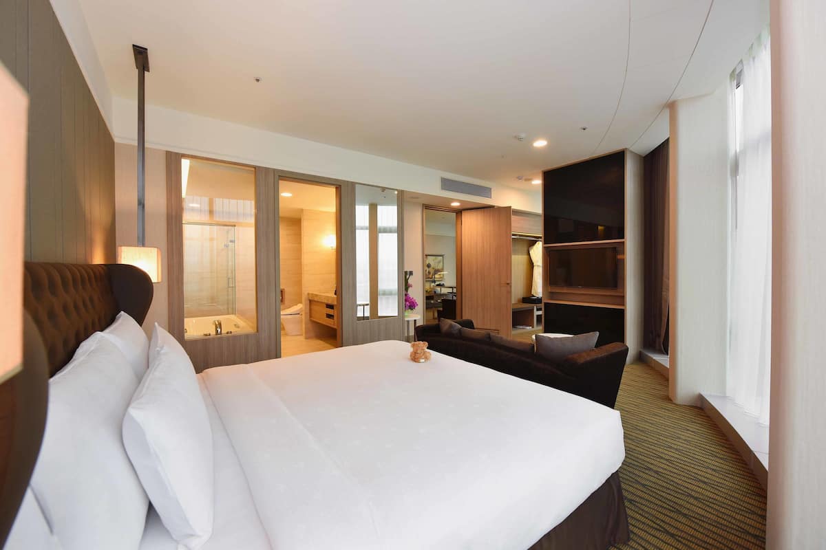 A hotel room with a large bed, a sofa, a desk, and a bathroom visible through an open door.