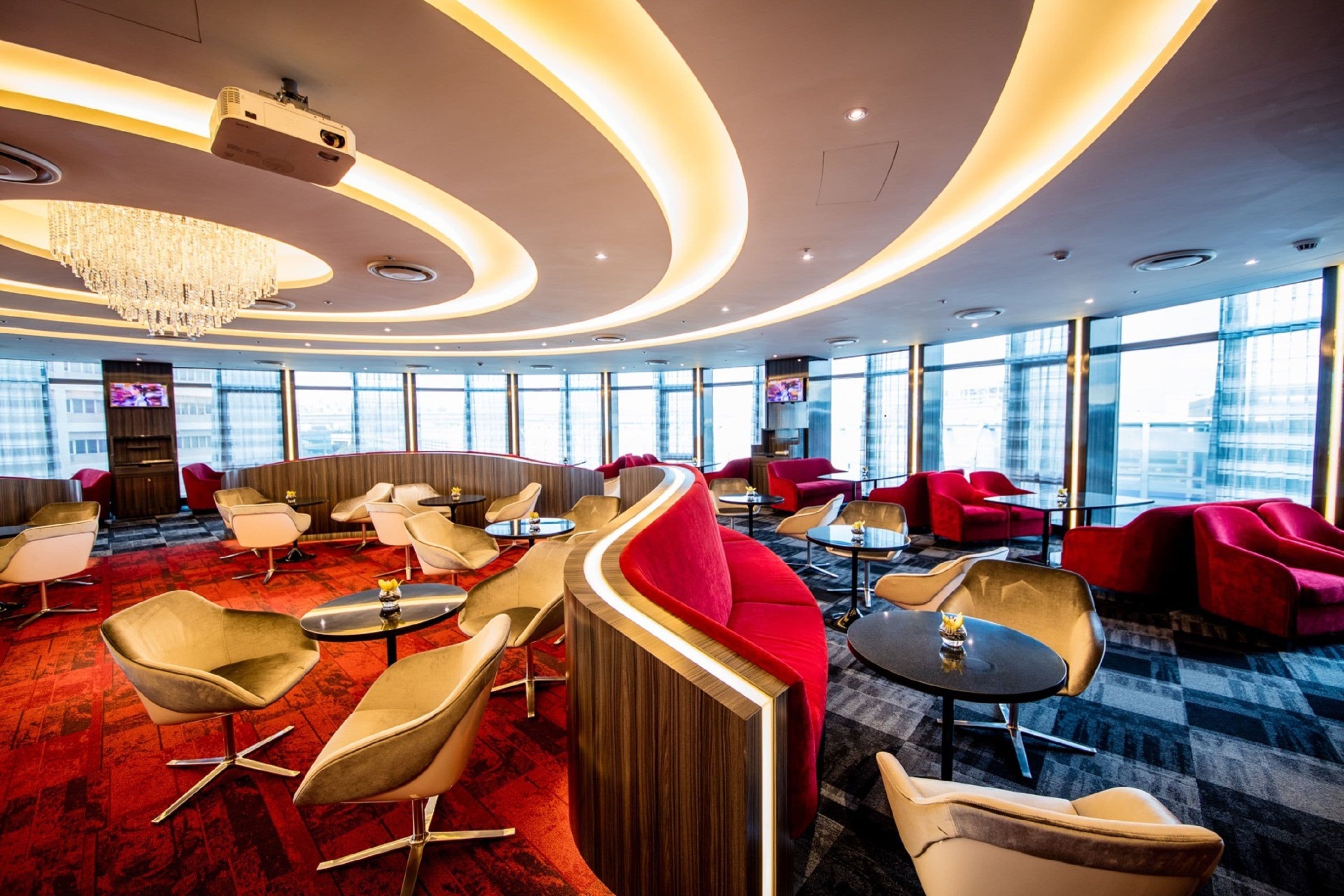 A modern lounge area with curved seating, a chandelier, and large windows offering city views.