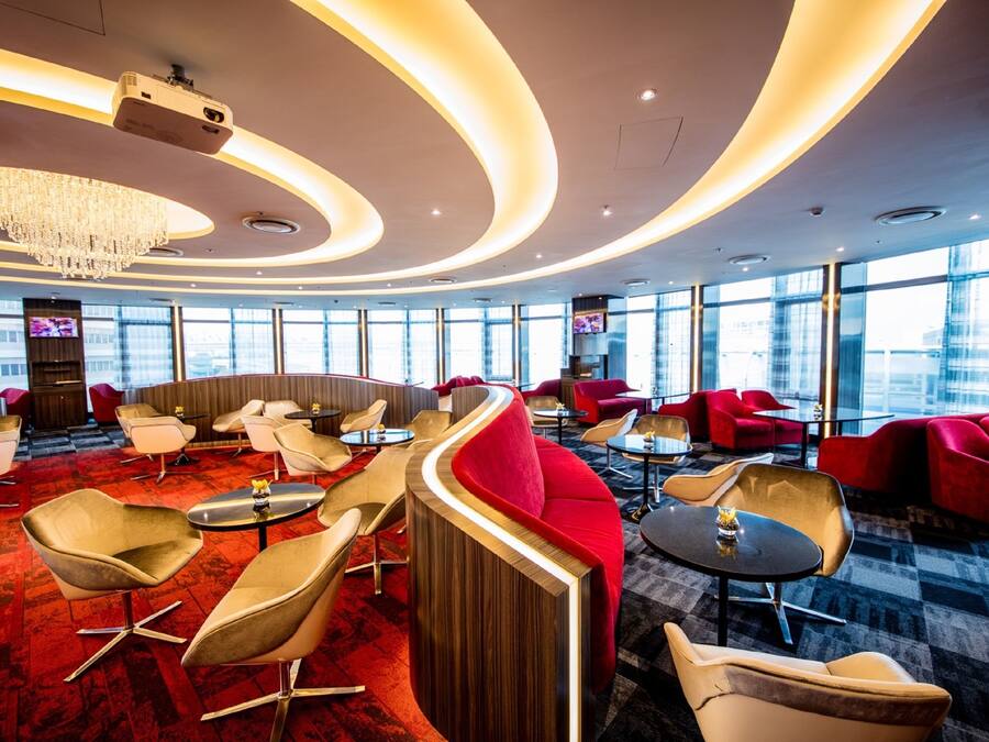 A modern lounge area with curved seating, a chandelier, and large windows offering city views.