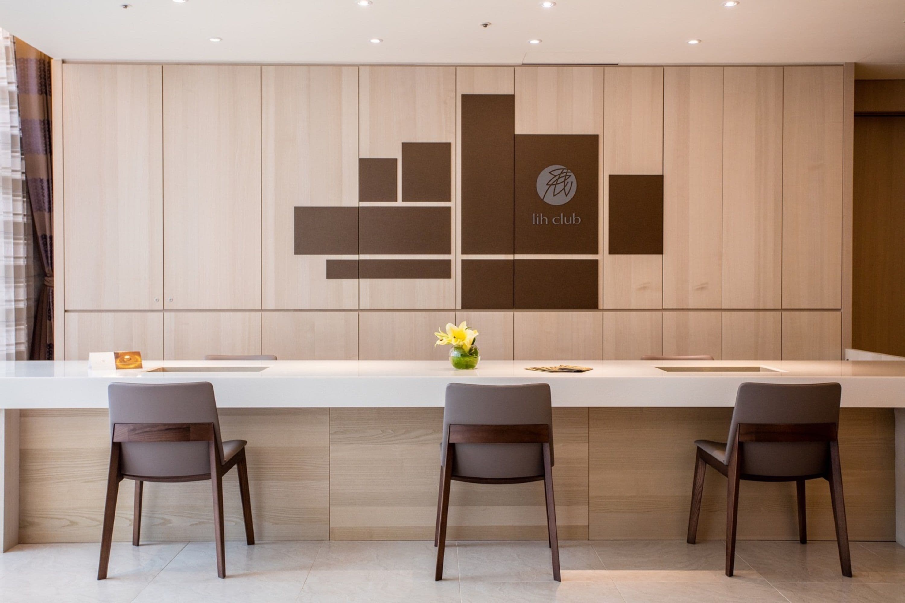 Een moderne hotel receptie met een wand van houtpanelen, een wit receptiebalie en drie grijze stoelen.