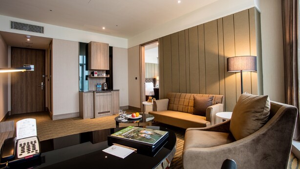 A hotel room with a kitchenette, a living area with a sofa and armchairs, a desk with a telephone and magazine, and a lamp. - Fullon Hotel Taoyuan Airport Access MRT A8 (Taoyuan City)