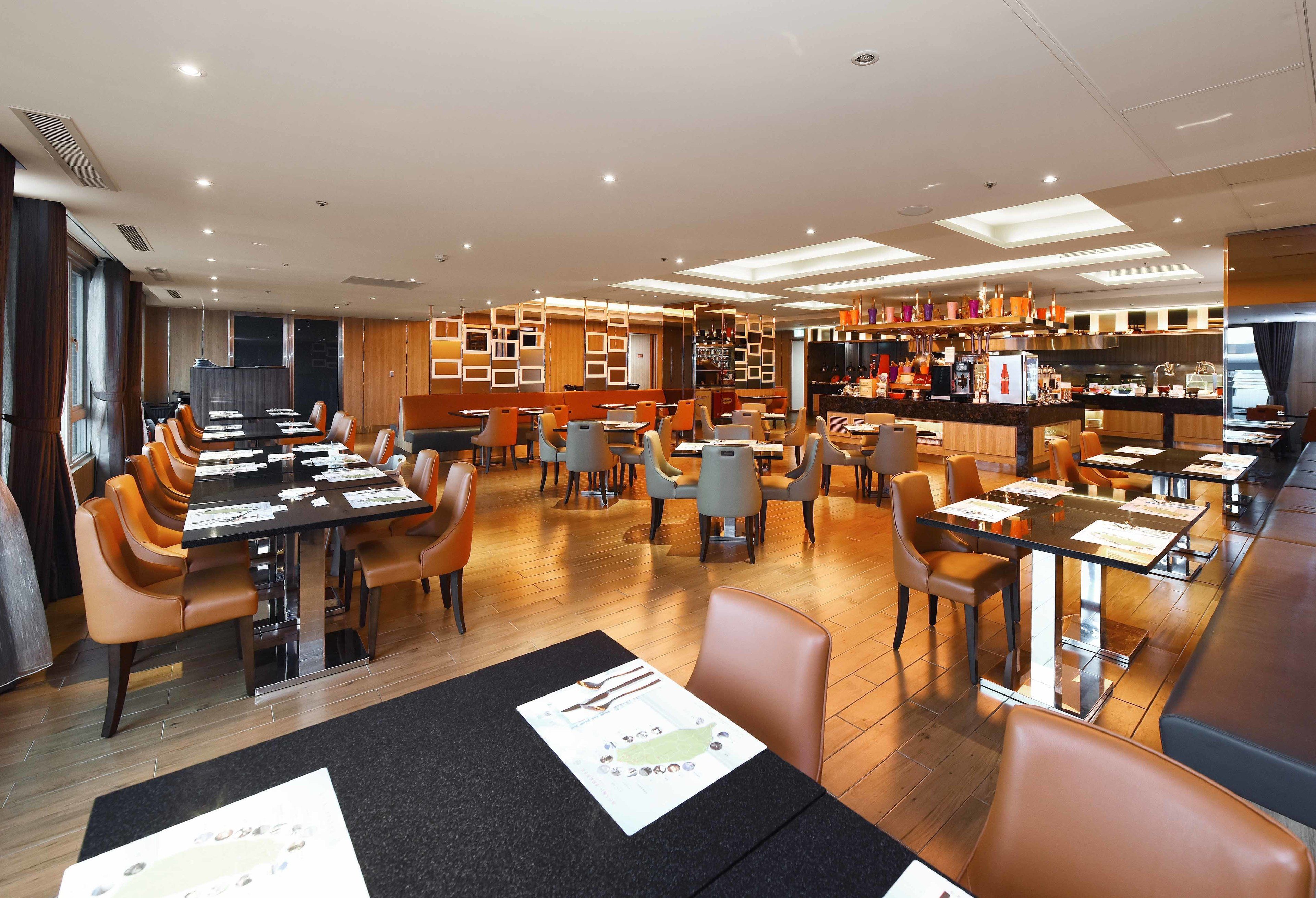 Un espace de restauration moderne dans un hôtel, avec de nombreuses tables et chaises, un bar et une cuisine en arrière-plan.