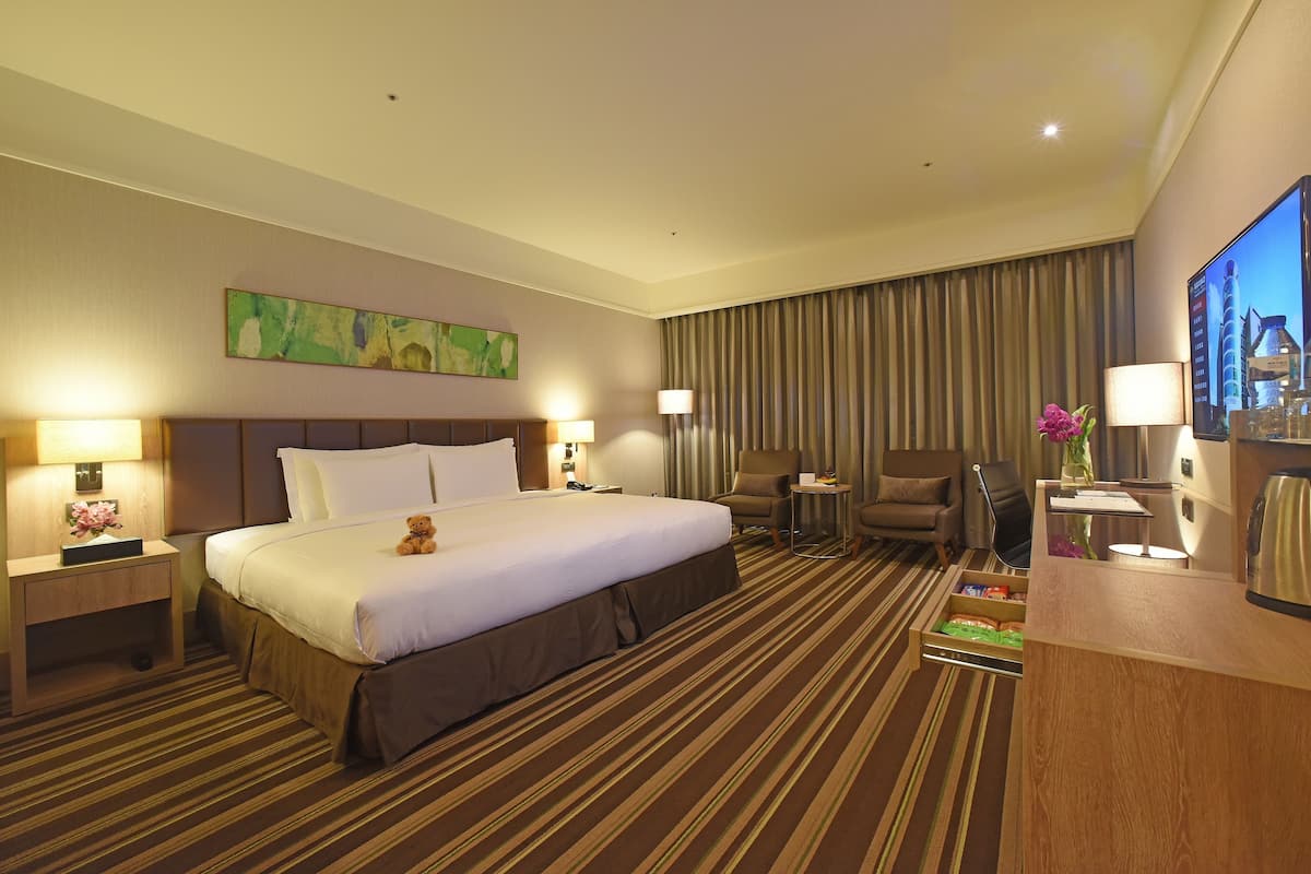 A hotel room with a large bed, two bedside tables with lamps, a chair, a desk with a computer, and a television.