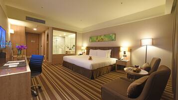 Habitación de hotel con cama, escritorio, silla, sofá, lámpara y televisor.