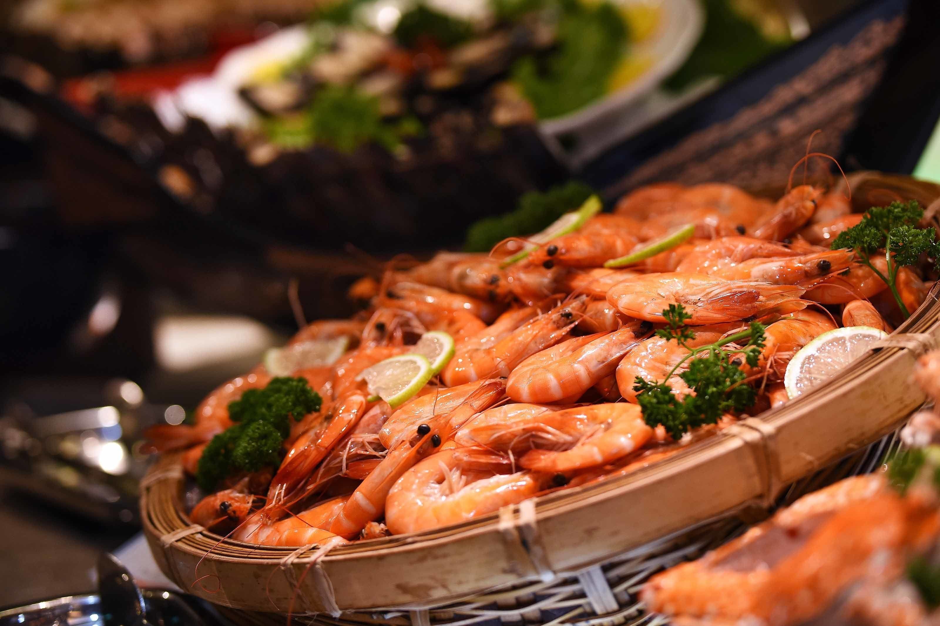 A basket filled with cooked shrimp garnished with parsley and lemon slices.