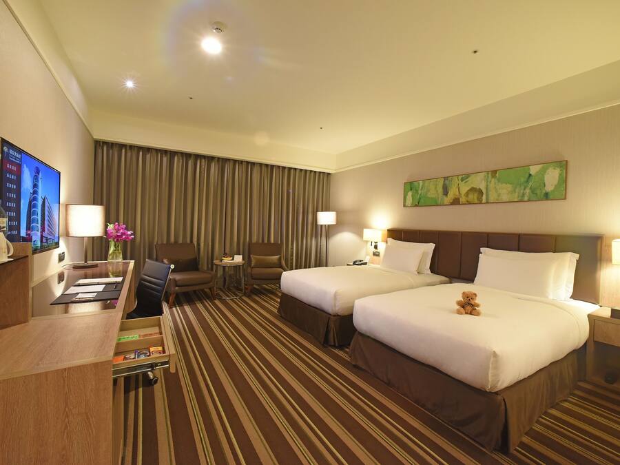 A hotel room with two beds, a desk with a computer, a TV, and a minibar.
