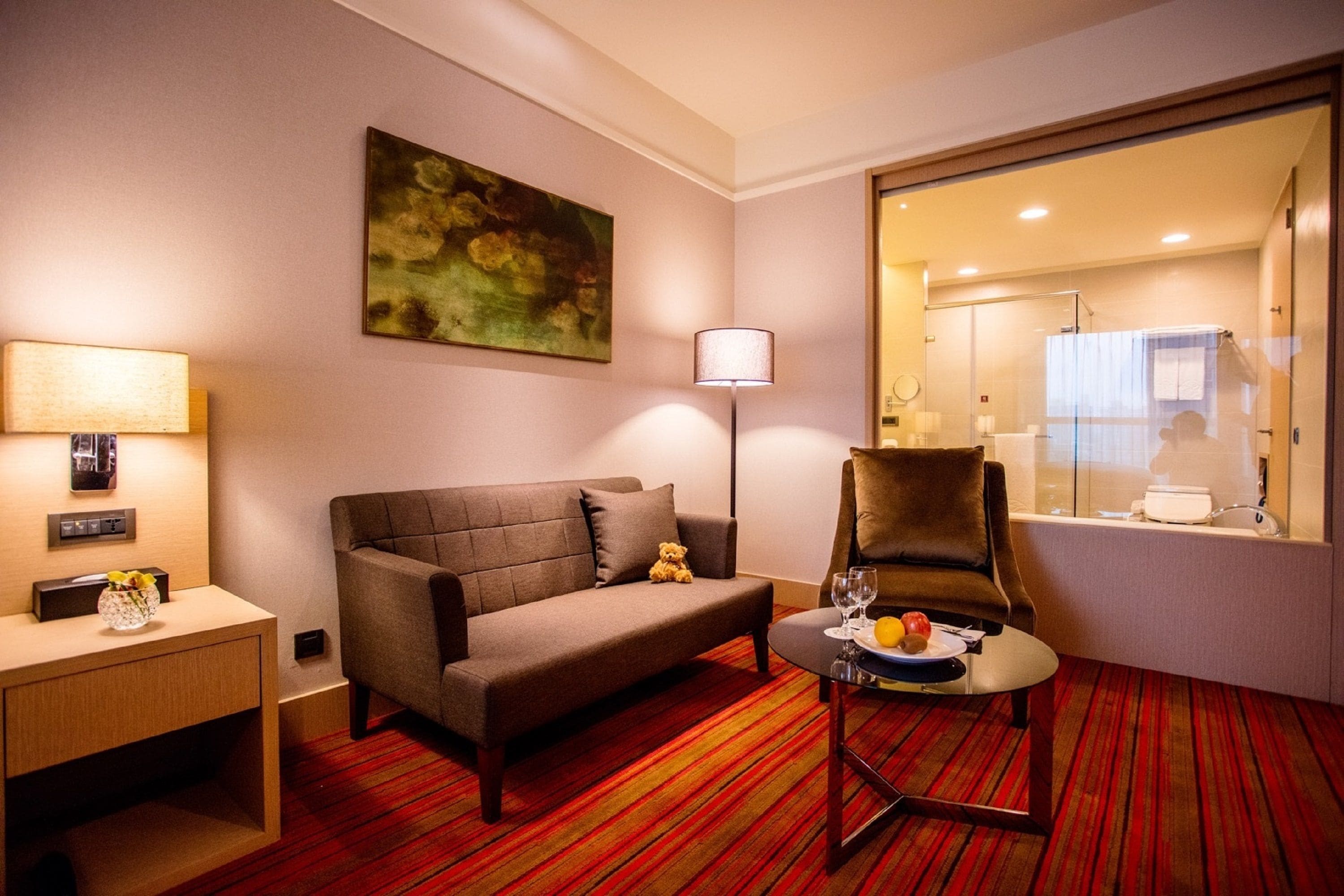 Een hotelkamer met een bank, fauteuil, klein tafeltje met fruit en een schilderij aan de muur.