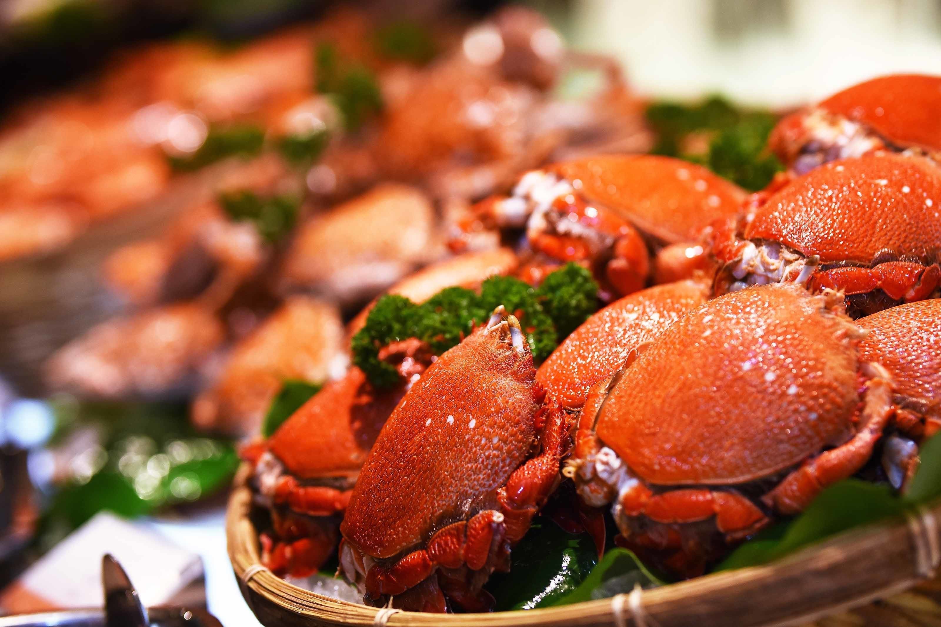 A close-up of a basket filled with cooked crabs, garnished with green leaves.