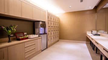 A modern kitchen with wooden cabinets, a refrigerator, a coffee machine, and a seating area with a long table and chairs.