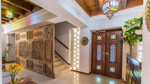Un hall d’entrée spacieux avec un escalier, des panneaux muraux décoratifs, une porte en bois ornée de vitraux et un vase rempli de fleurs.