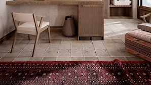 Une chambre moderne avec un plafond en bois, un téléviseur à écran plat fixé au mur, un bureau en bois, une chaise, un tapis rouge à motifs et une fenêtre avec vue.