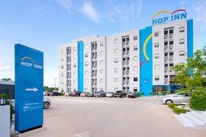A modern hotel with a blue and white color scheme, multiple floors, and a parking lot with several cars.