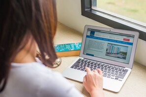 A person using a laptop on a wooden desk with a window in the background.