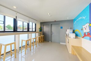 A clean, modern reception area with a counter, wooden stools, and a colorful mural. - Hop Inn Roi Et (Roi Et)