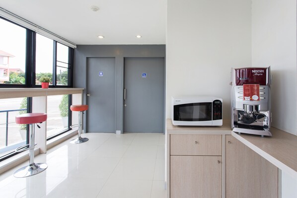 A modern kitchen with a microwave and coffee machine, two red bar stools, and a view through large windows.