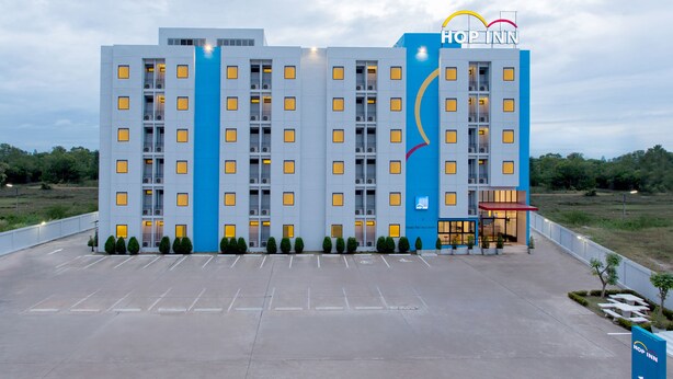A modern hotel with a blue and white facade, multiple floors, and a parking lot in front. - Hop Inn Roi Et (Roi Et)