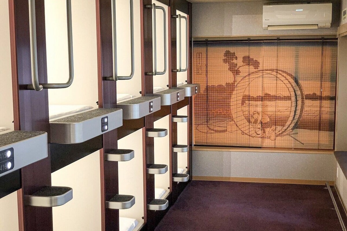 Eine Reihe von Stockbetten mit Metallgitter und einem traditionellen japanischen Bildschirm mit Landschaftsmotiv.