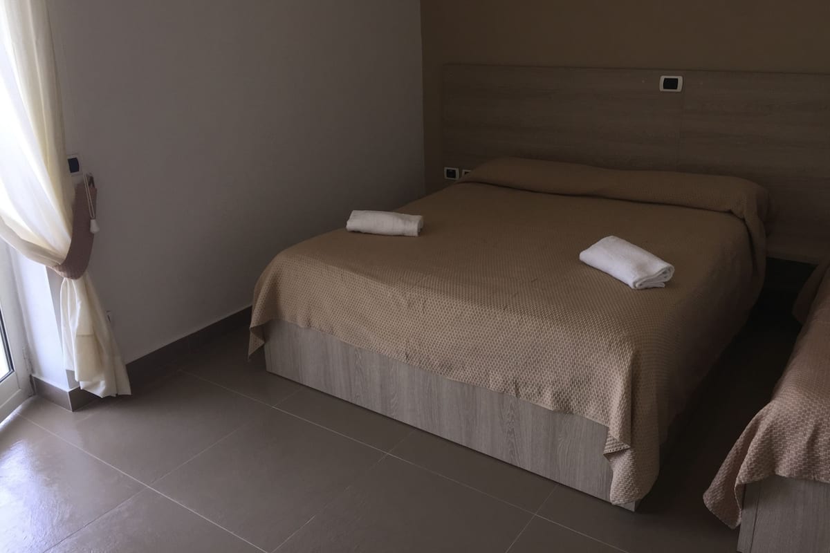 Ein Hotelzimmer mit einem großen Bett, einem Nachttisch und einem Fenster mit Vorhängen.