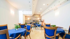 A dining area with blue tablecloths and wooden chairs, a kitchen in the background, and a ceiling with recessed lighting. - Hotel Stella Maris Terme & Beauty (Casamicciola Terme)