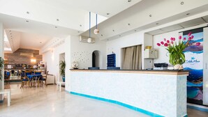 A hotel reception area with a central counter, a dining area with blue chairs, and a large window with a view of the sea. - Hotel Stella Maris Terme & Beauty (Casamicciola Terme)