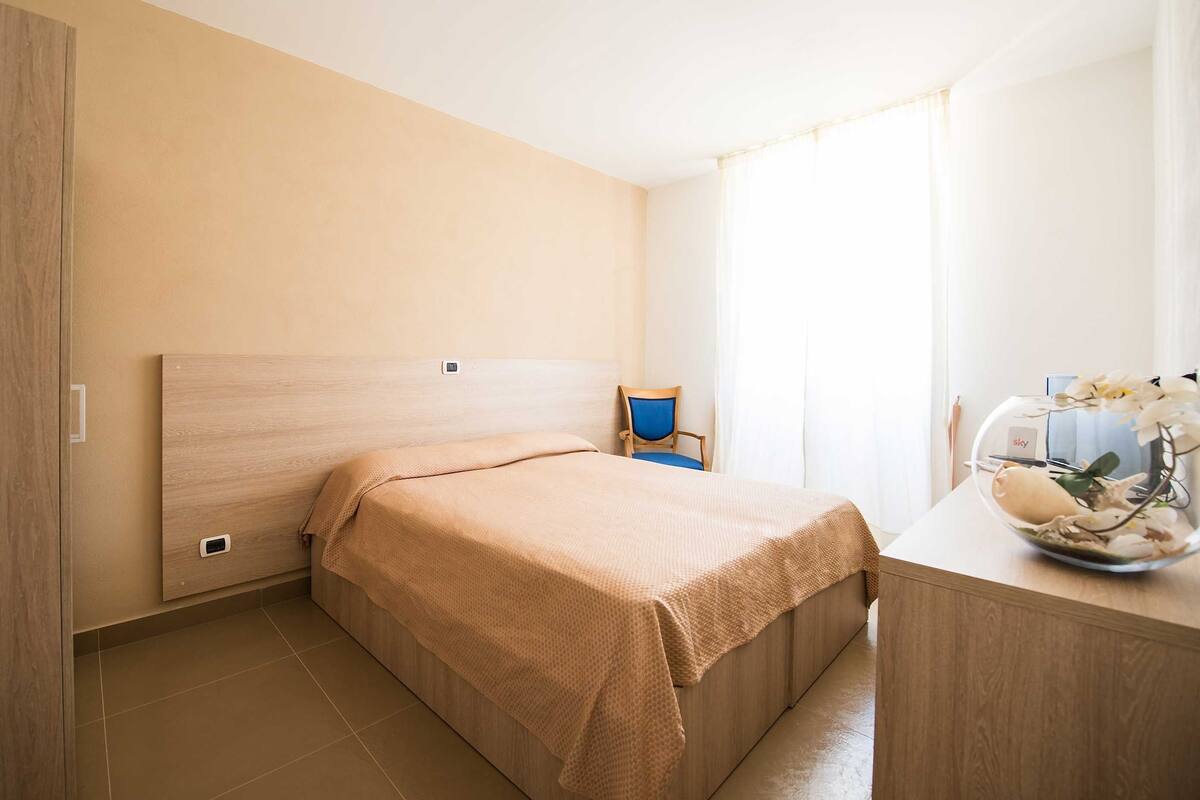 Ein Schlafzimmer mit Bett, Stuhl, Schreibtisch und einem Fenster mit Vorhängen.