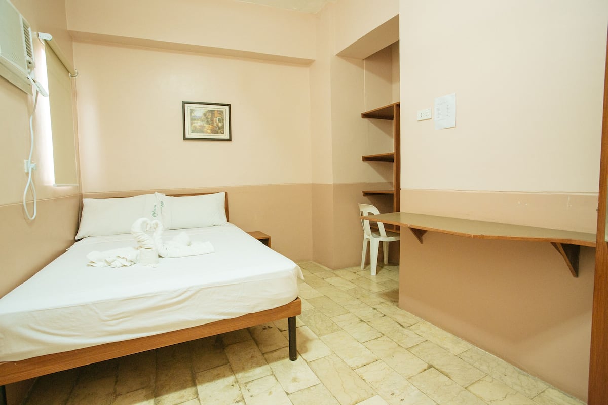 A small, neatly arranged bedroom with a single bed, a chair, and a shelf unit.