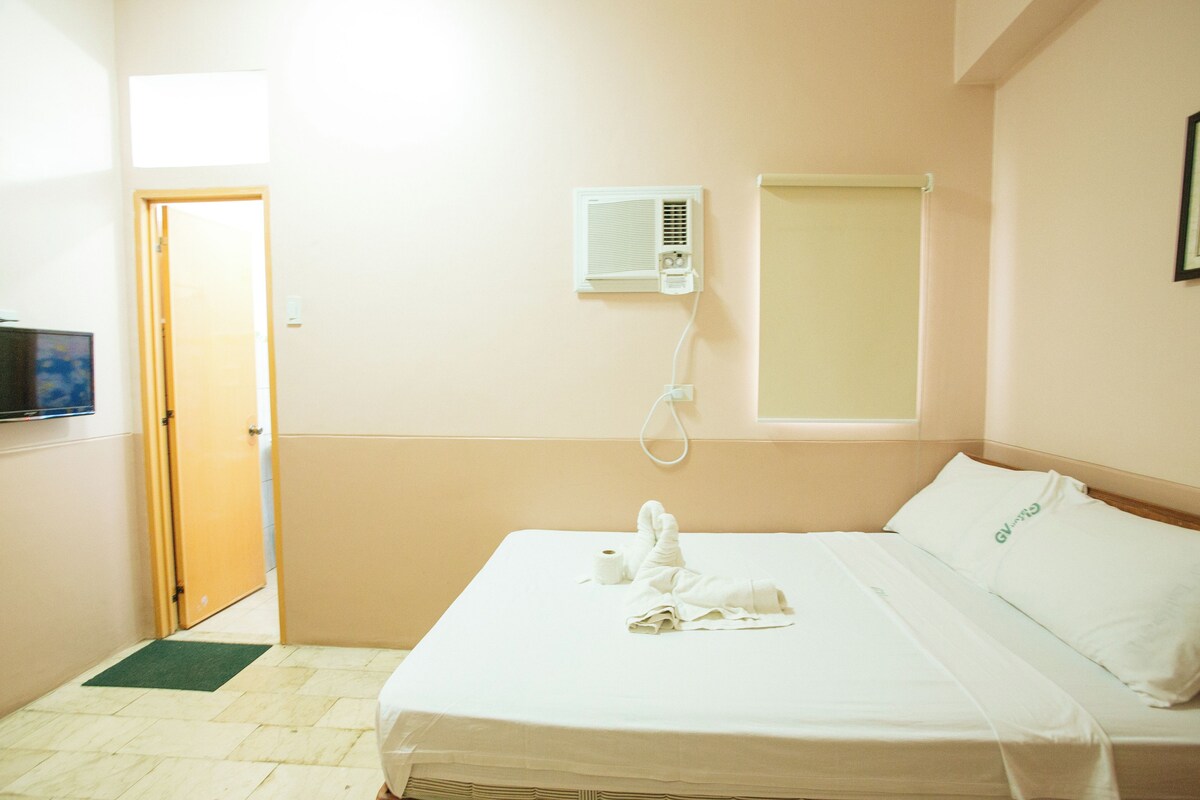Una habitación de hotel con cama, aire acondicionado instalado en la pared, ventana y puerta.