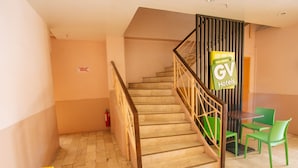 A hotel interior with a staircase, a reception desk, and green chairs.