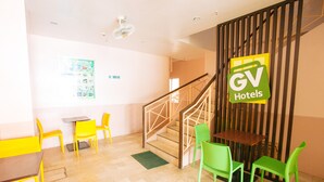 A hotel lobby with a staircase, yellow and green chairs, a wooden table, and a 'No Smoking' sign.