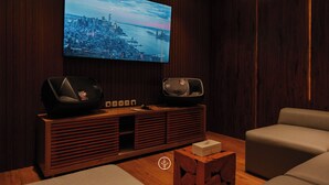 Una sala de estar moderna con un televisor de pantalla plana grande montado en una pared de madera, un mueble de madera para entretenimiento con altavoces y un sofá color beige.
