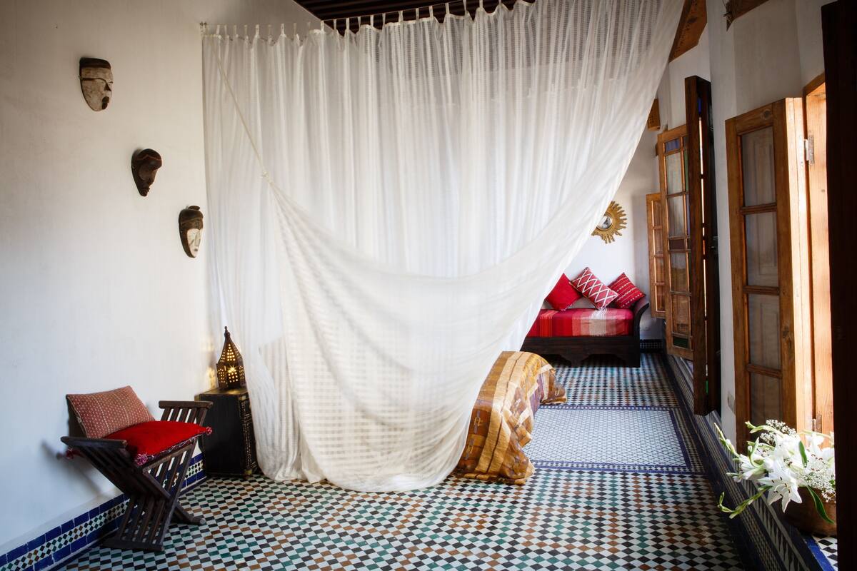 A room with a checkered floor, a red cushioned chair, a white curtain, and a wooden door.