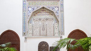 A traditional Moroccan interior with a patterned tile floor, a wooden sofa with cushions, and a large decorative door.