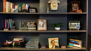 Una estantería con libros, un teléfono antiguo, una foto enmarco, una bicicleta y una radio.