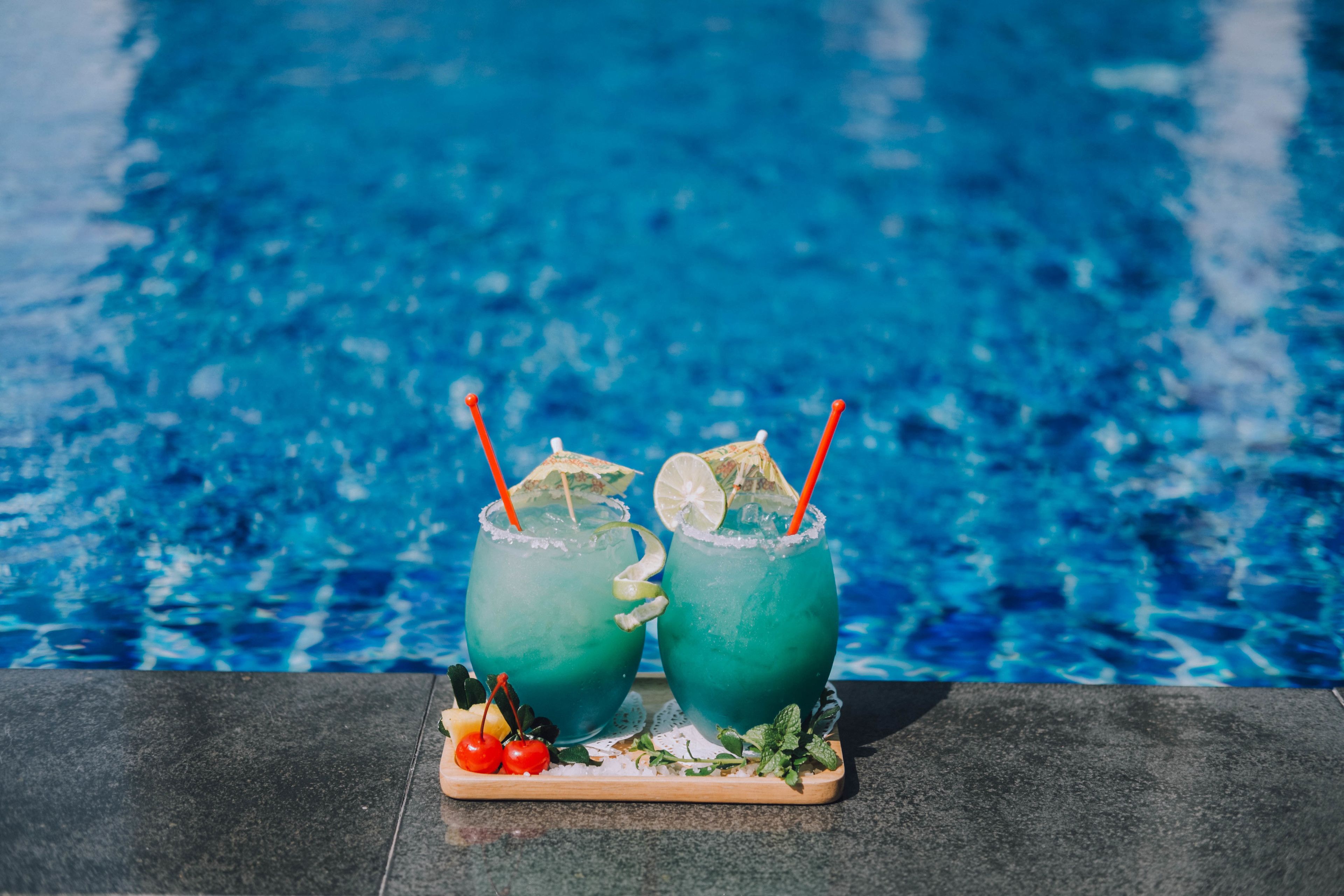 Dos bebidas con pajitas y rodajas de lima sobre una bandeja junto a una piscina.