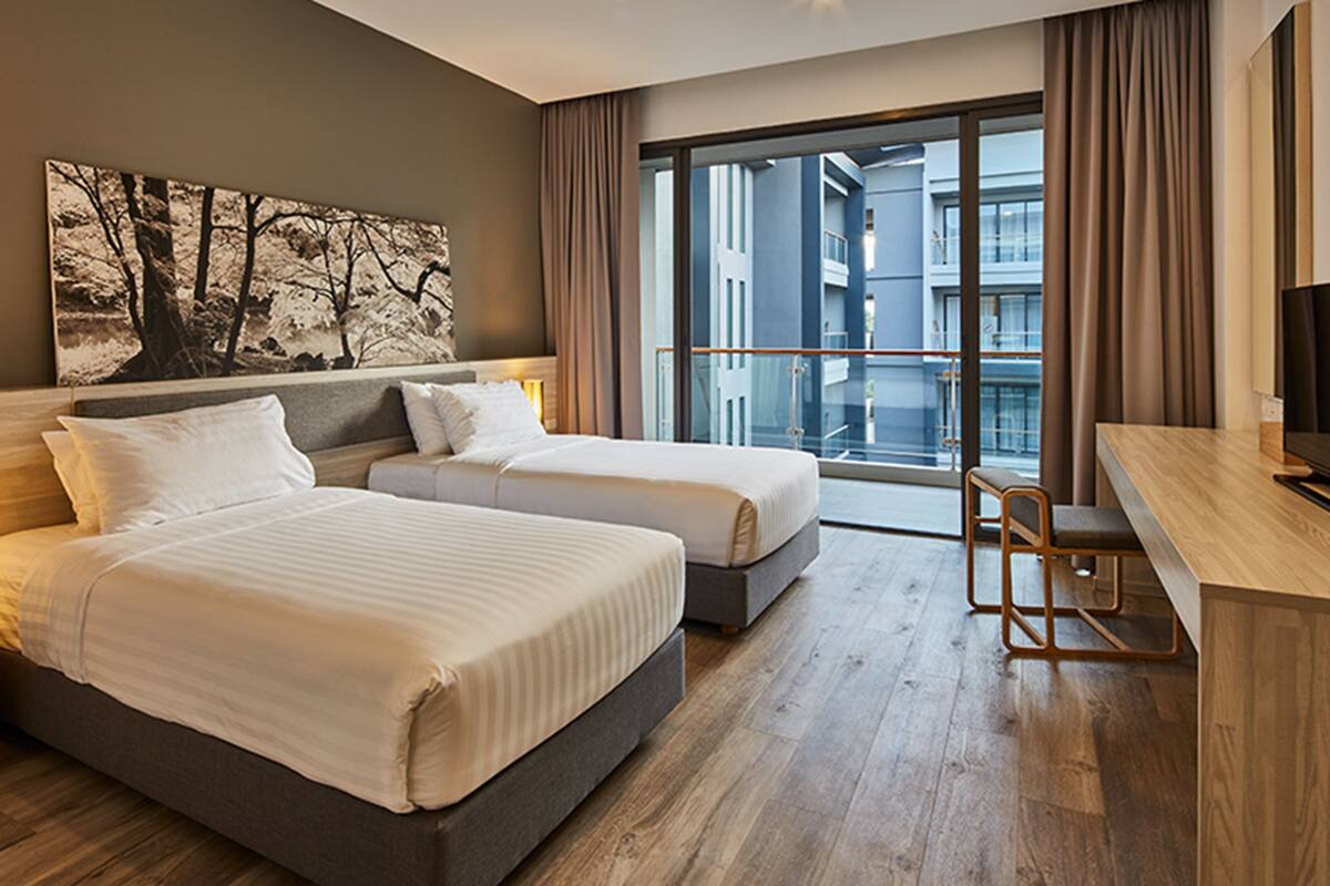 Une chambre d’hôtel moderne, dotée de deux lits, d’un bureau et d’une grande fenêtre donnant sur la ville.