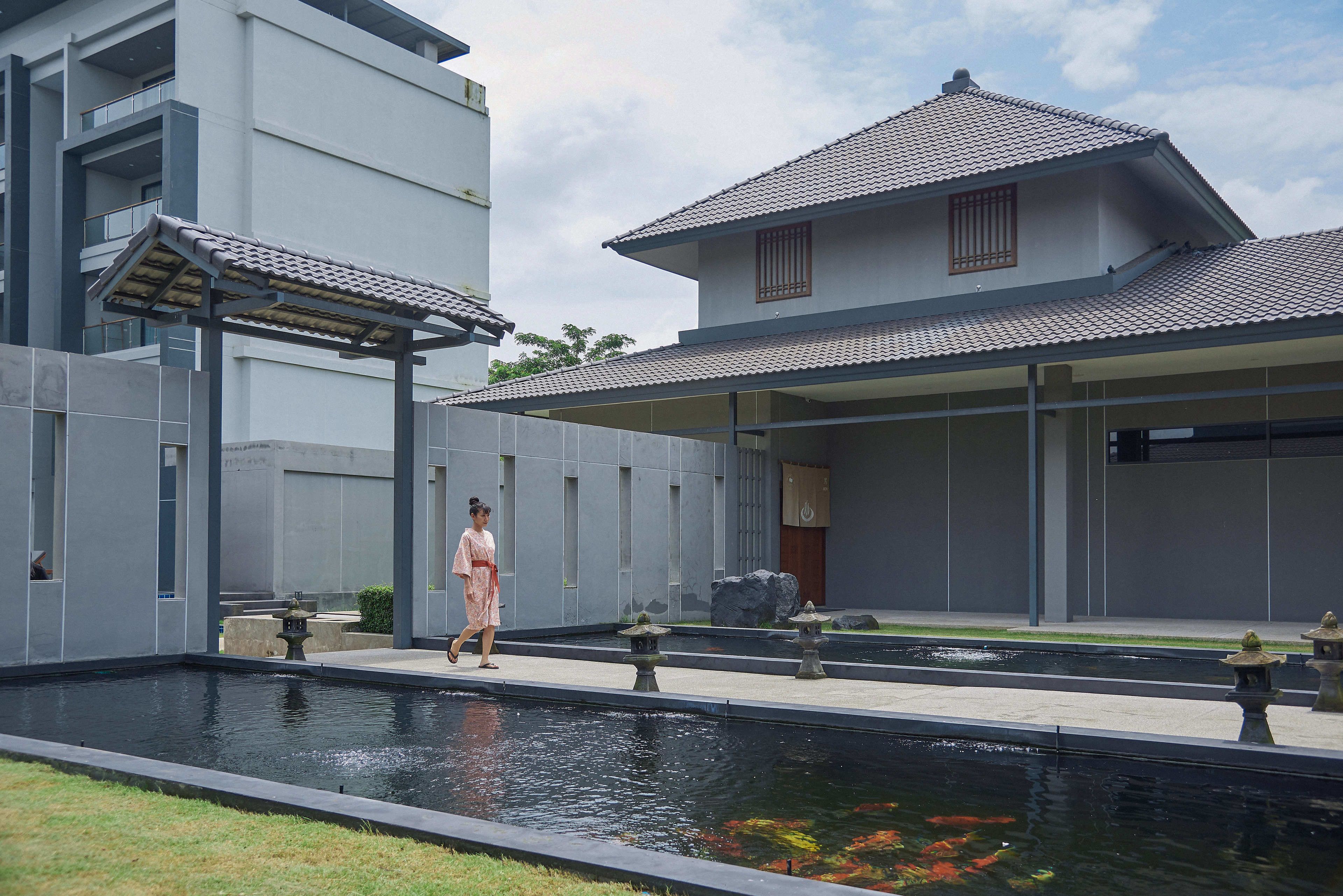 A modern building with a traditional tiled roof, a koi pond, and a stone lantern.
