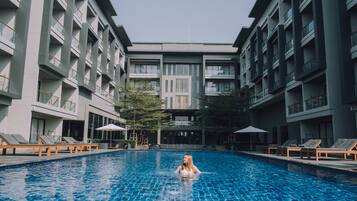 Una piscina con sillas de descanso y un edificio con balcones al fondo.