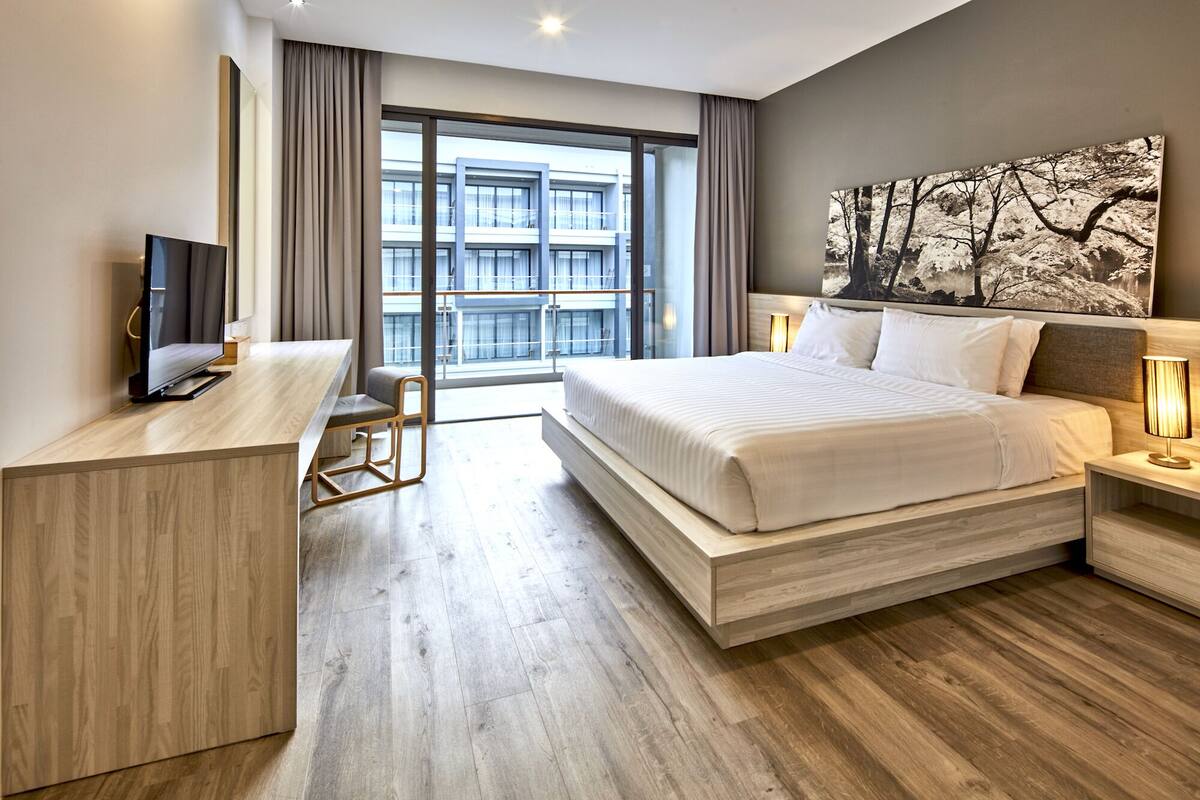 Une chambre d’hôtel moderne dotée d’un grand lit, d’un bureau, d’une télévision et offrant une vue sur le paysage urbain grâce à de grandes fenêtres.