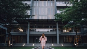 A woman walking towards a modern building with a glass facade and a set of stairs leading to the entrance. - Serenity Hotel Spa & Onsen (Kabin Buri)