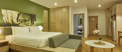 A modern bedroom with a bed, bedside tables, a sofa, a small table with a plant, and a bathroom visible through an open door.