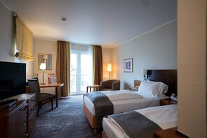 A hotel room with two beds, a desk with a chair, a television, and a large window with curtains.