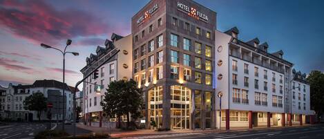 Um hotel moderno com entrada imponente, vários andares e fachada bem iluminada.