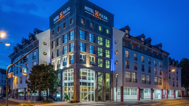 A modern hotel with a prominent 'HOTEL FULDA' sign, large windows, and a well-lit entrance. - Hotel Fulda Mitte (Fulda)